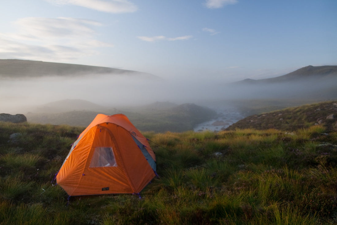 A little orange tent sits on a hill overlooking a misty winter valley