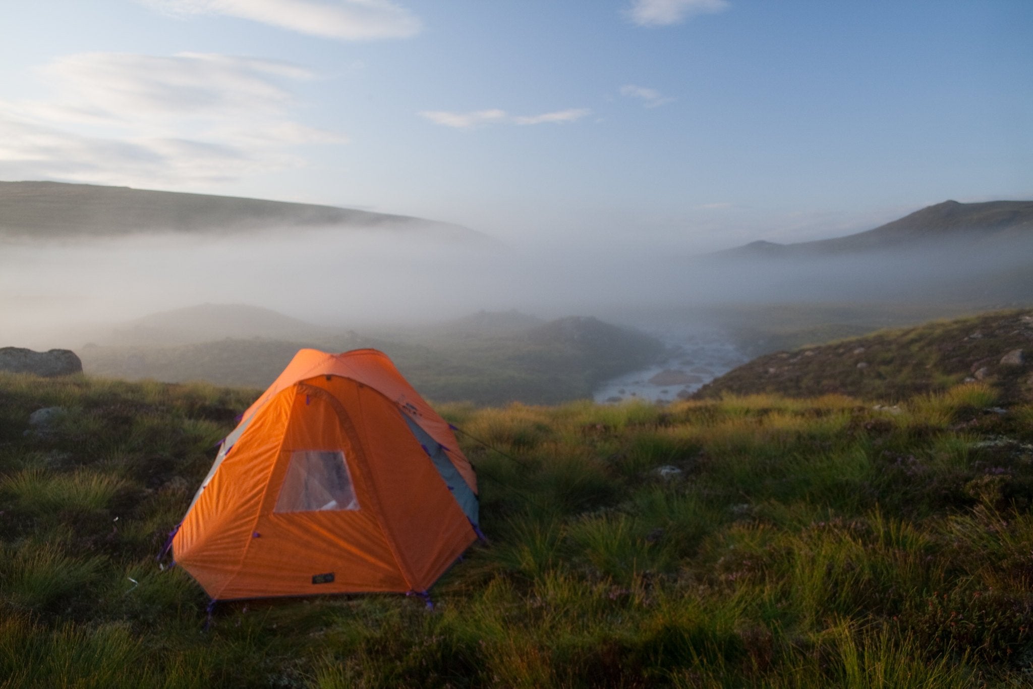 A little orange tent sits on a hill overlooking a misty winter valley